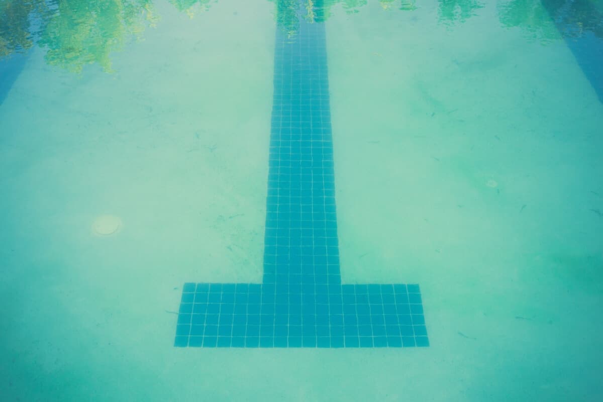 A tiled lane marker on a pool floor, seen through hazy green-tinted water