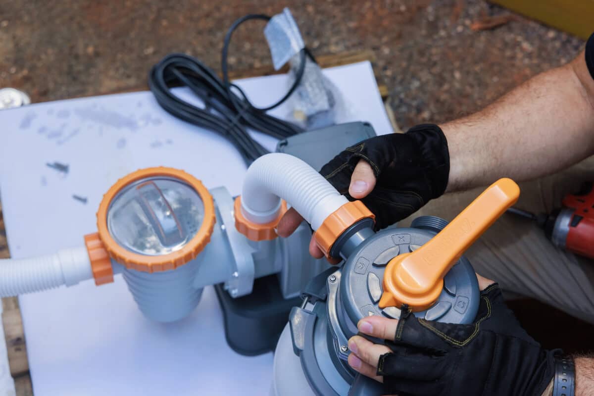 Gloved hands fitting a hose to the multiport valve on a pool pump