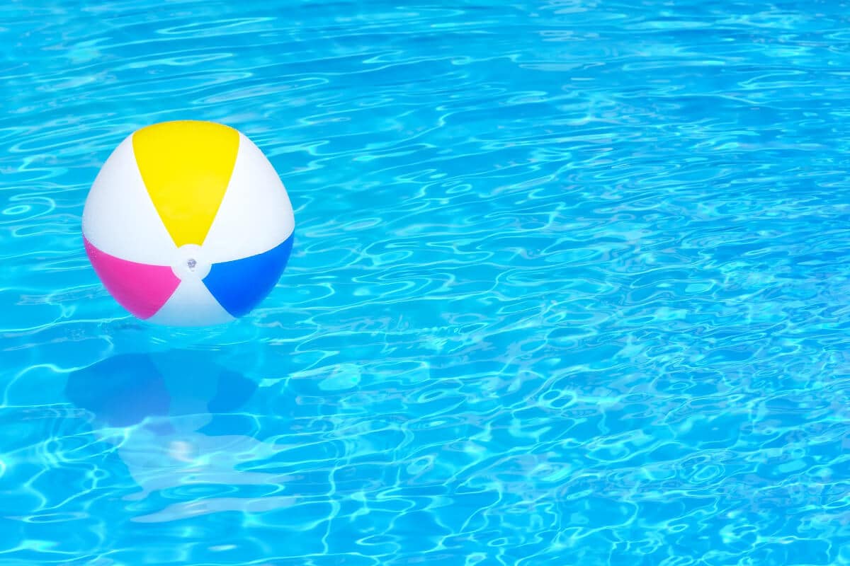 A striped beach ball floating on bright blue, sunlit pool water